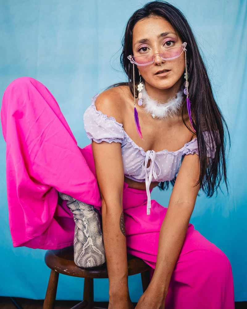 Customer @andreaelenaa_ wearing lilac sunglasses with dangling purple feathers, a lilac off-the-shoulder top, hot pink trousers, and snakeskin boots Customer @andreaelenaa_ wearing lilac sunglasses with dangling purple feathers, a lilac off-the-shoulder top, hot pink trousers, and snakeskin boots