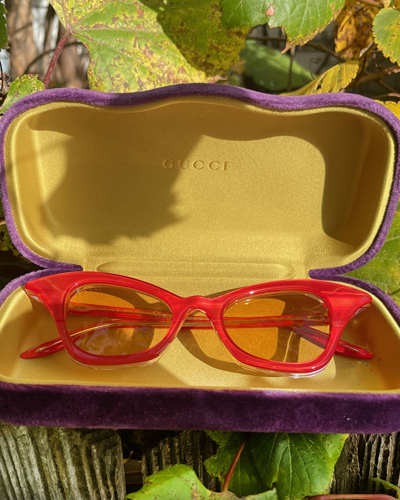 A pair of translucent red Gucci cateye glasses in sit in their yellow and purple case