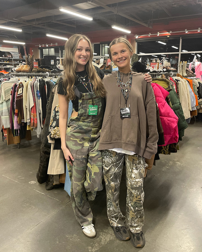 Two women wearing camouflage pants standing in middle of clothing store